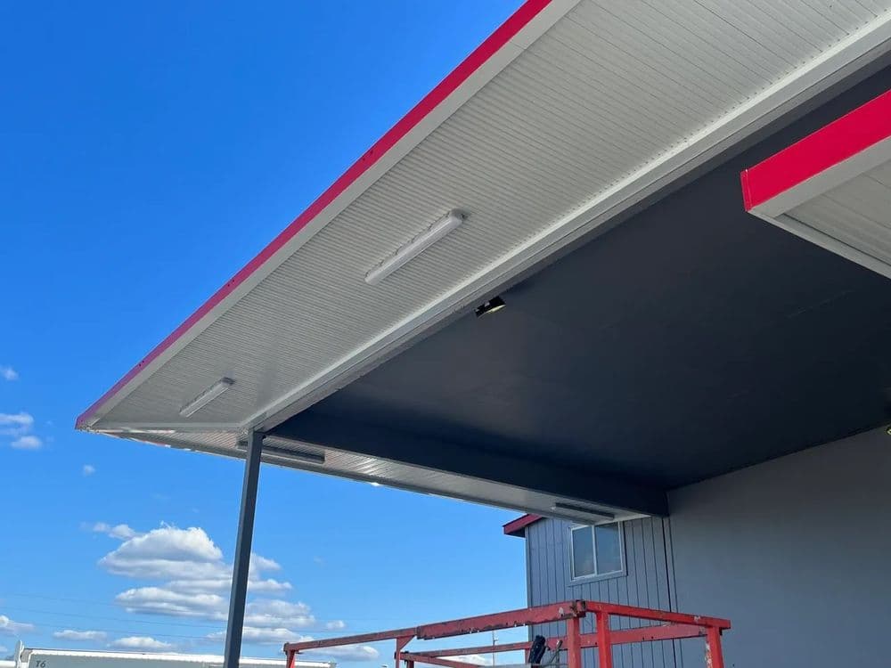 Roof overhang with LED lights, blue sky, and modern building in background.