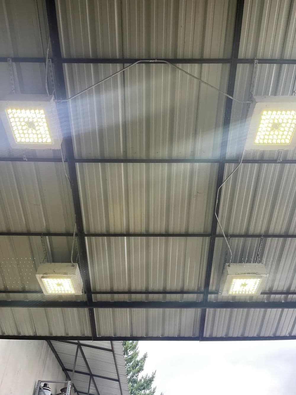Bright LED lights illuminate a metal roof structure in a warehouse setting.