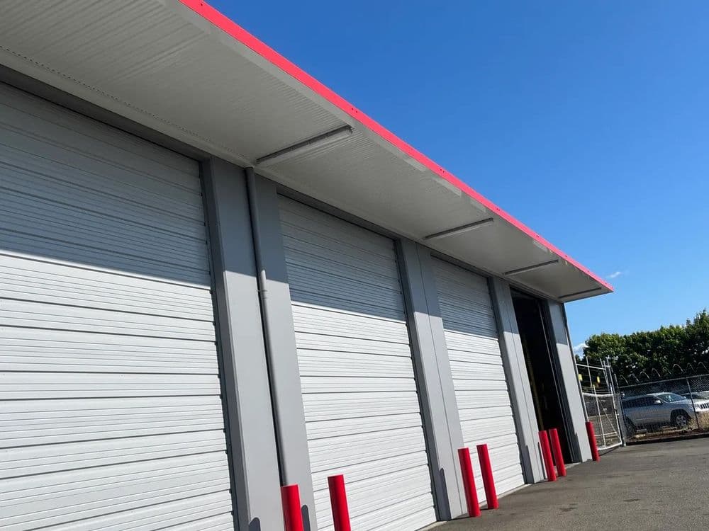 Modern storage facility exterior with gray metal doors and red accents against a blue sky.