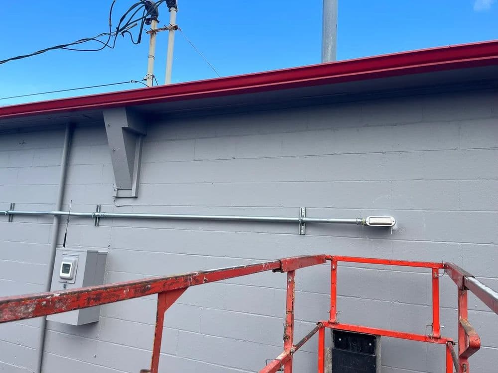 Scaffolding in front of a gray building with red trim and electrical conduit.
