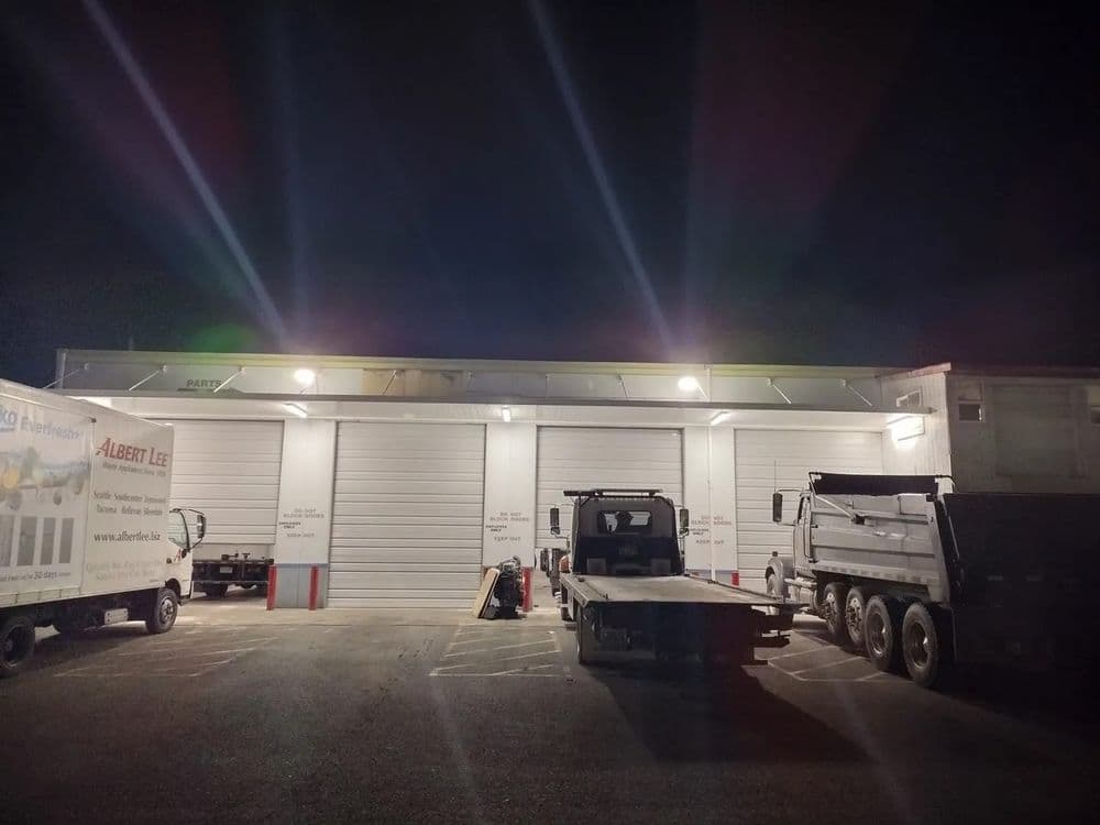 Nighttime view of a loading dock with trucks and storage units, illuminated by overhead lights.