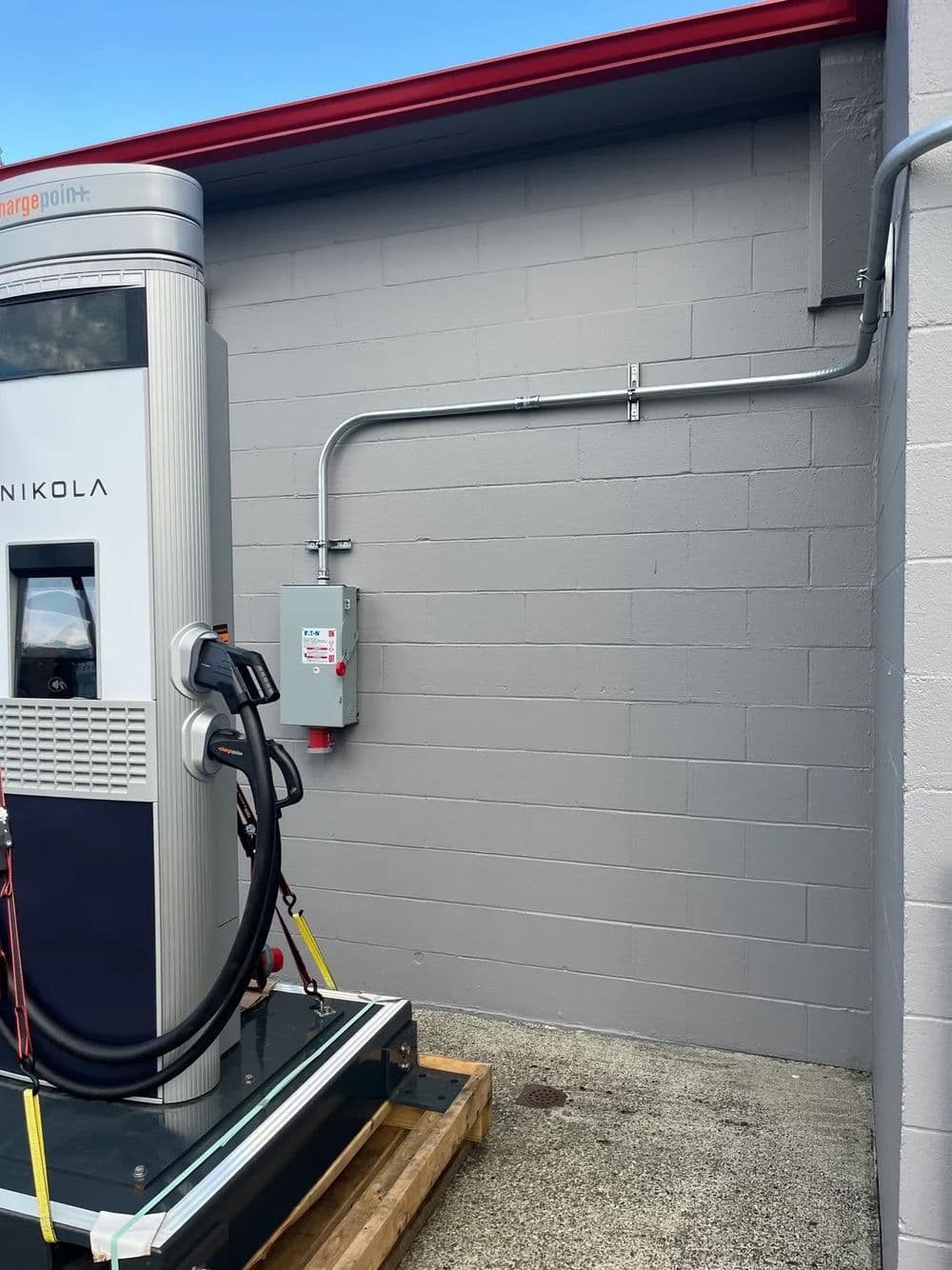Nikola electric vehicle charging station installed on a gray wall with power supply connection.