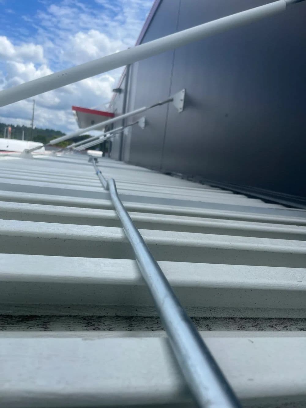 Metal rods and brackets mounted on a white surface against a cloudy sky background.