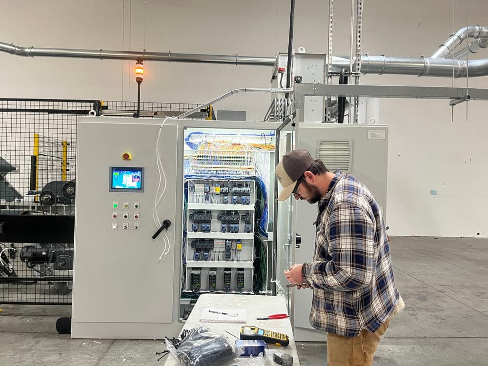 Technician working on industrial control panel in a spacious warehouse setting.
