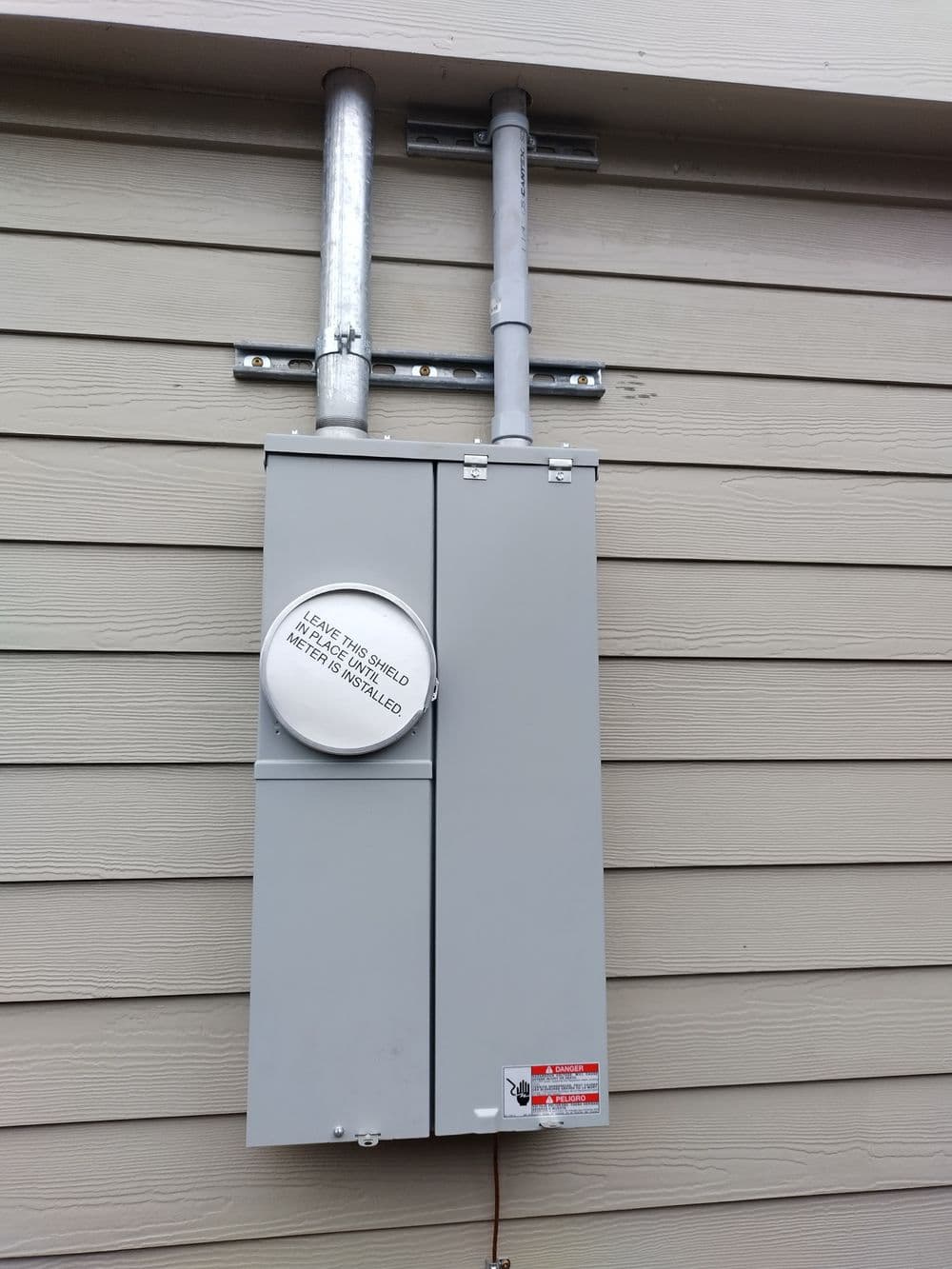 Electrical utility meter installed on wooden exterior wall with protective shield.